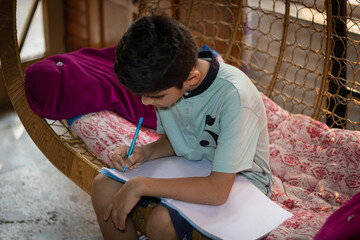Fototapeta premium A young boy is writting on a note book while sitting in a cradle at home
