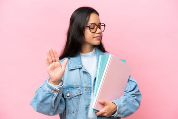 Young student Colombian woman isolated on pink background making stop gesture and disappointed