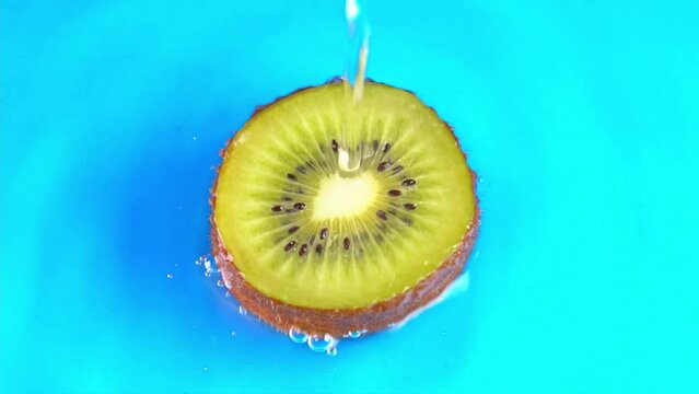 Water pours on green hue juicy kiwi fruit on cyan background