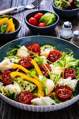 Fish salad - fried halibut fillet with fresh vegetables on wooden table
