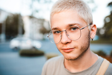 Handsome young man with blond short cut hairstyle wear glasses over urban city background outdoor....