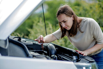 The woman pulls out a probe in her car engine to check the oil level. The woman manages the car herself