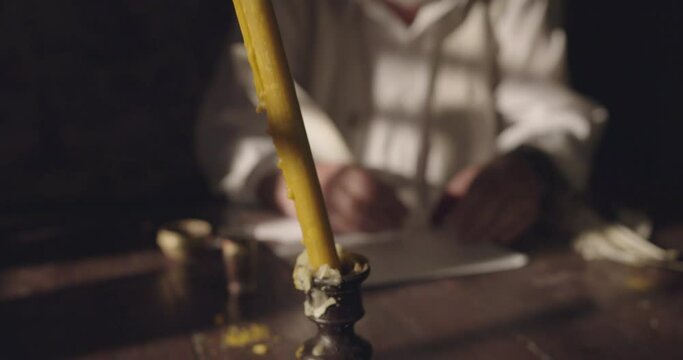 Handwriting  with a feather on papyrus of male person with candlelight, crane shot, shallow depth of field.