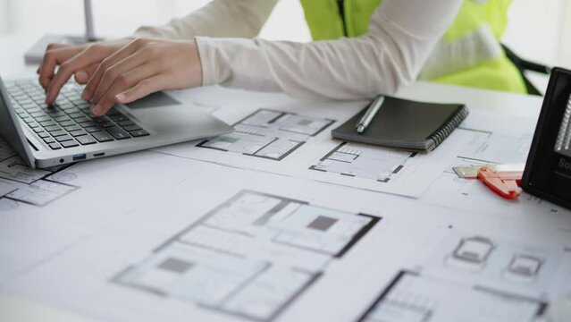 Close up of hands working and calculations on laptop and floor plan drawings about design architectural and engineering for houses and buildings.