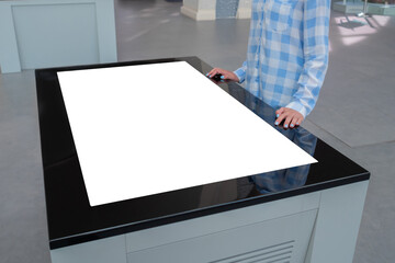 Woman in blue plaid shirt looking at blank interactive touchscreen white display of electronic table kiosk at exhibition or museum. White screen, mock up, copyspace, template, technology concept.
