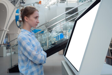 Woman in blue plaid shirt looking at blank interactive touchscreen white display of electronic...