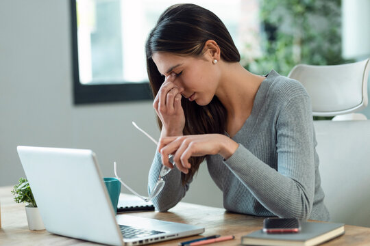 Stressed business woman working from home on laptop looking worried, tired and overwhelmed.
