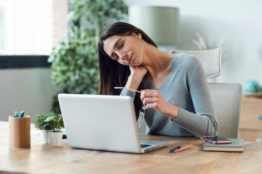 Tired business woman with neck pain looking uncomfortable while working with laptop at home.
