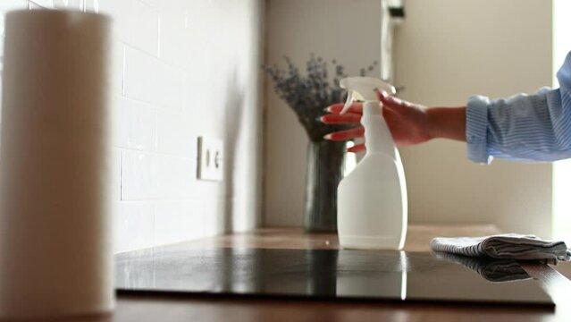 Delicate cleaning induction electric stove. Housewife cleans kitchen hob with cleaning spray with mockup and paper towels. Woman cleaning house. Housework cleaning service, household chores.