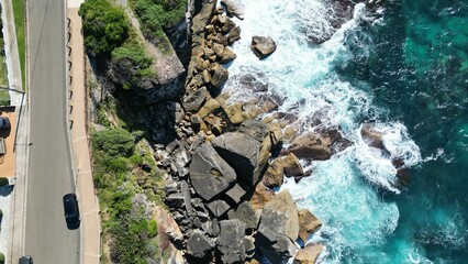 Aerial view of blue sea waves hitting the rocky shore near a road with a car