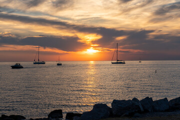 Sonnenuntergang am Meer mit Segelbooten im Hintergrund und Steinen im Vordergrund