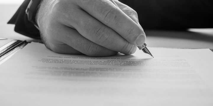 Monochrome image of a lawyer signing a legal document with a pen