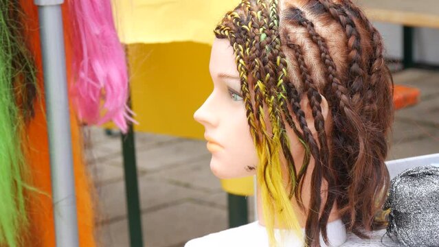 Hairdressing training wig head, lots of African multi-colored braids on the background of artificial hair curls in the street