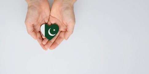 The national flag of Pakistan in the shape of a heart of arms in female hands. Flat lay, copy space.