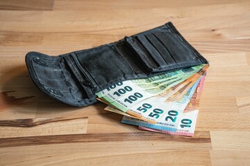 Picture of a black wallet on a wooden surface with Euro banknotes sticking outside