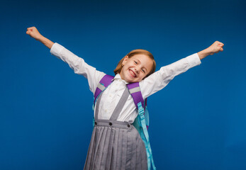 A joyful, excited teenage girl, clenching her fists, is genuinely happy and laughing loudly on a blue background. A pretty schoolgirl is smiling. The concept of children's happiness.