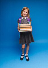 a happy teenage girl in a school uniform holds a stack of books. Banner of a schoolgirl. Portrait of a schoolgirl with space to copy on a blue background.