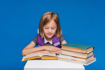 The little schoolgirl raised her hand to answer the question. a schoolgirl with books on a blue background.