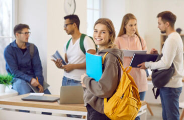 Fototapeta Portrait of smiling millennial Caucasian girl with backpack with groupmates in college or university. Happy young female schoolgirl satisfied with school course or training. Education concept. obraz