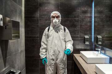 A man with brown eyes in the white protective suit is preparing to disinfect the space in the public restroom.Pandemic control, COVID19 outbreak situation