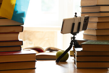 The phone on stands stands on the table near books and notebooks next to the flag of Ukraine,...