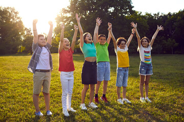 Happy children raise their hands together laughing and shouting happily during fun in park. Preteen boys and girls in summer casual clothes having fun outdoors. Concept of happiness, gladness and fun.