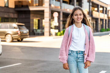 Fototapeta premium A young teenage girl goes to school with a backpack. A teenage student or a schoolgirl. The concept of education. Happy girl's face, positive and smiling emotions.