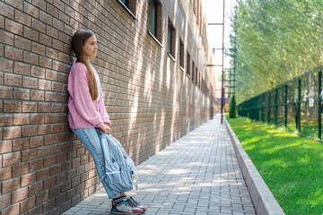 A cute schoolgirl girl is standing against a brick wall in the backyard of the school