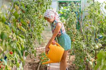 A young teenage girl in a rustic shawl is watering a vegetable garden in a greenhouse with a watering can