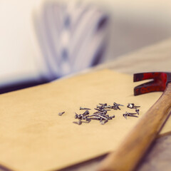 Slightly high angle view from perspective of the head of an iron hammer next to some small metal nails on a wooden board and selective light on them
