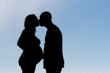 silhouette of couple expecting pregnant baby with clouds in the background.