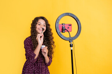 smiling child with long curly hair making video for blog hold powder brush