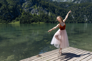 Fototapeta na wymiar Young ballerina dancing on a wooden stage by the lake