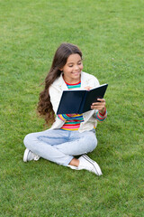 glad teen girl making notes in notebook sitting on grass. taking notes. student make notes outdoor