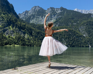 A young ballerina dances on a wooden stage by the lake against the backdrop of the Alpine mountains © Guzel
