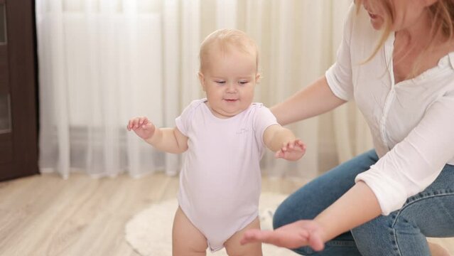 Slow motion of Caucasian cute baby girl boy child learn to walk with parent. smiling young mother support toddler infant taking first step walk on floor in living room at home. happy family concept.