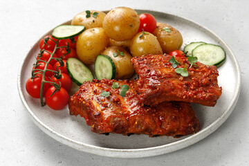 Dish, plate with Marinated pork bbq ribs, young potatoes, tomatoes on ceramic plate and grey background. Hearty Dinner, lunch, meal.