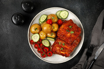 Dish with young potatoes, tomatoes and Marinated pork bbq ribs on black  dark background. Top view. Dinner, lunch.