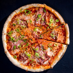 Delicious pizza with mozzarella cheese, ham, leeks on a tomato base on black background
