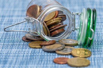 Small coins in euro cents are poured out of a glass jar on a textured blue background, close-up, selective focus. A concept for business and finance.
