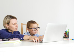 A woman shows a task to a boy in glasses on a laptop and teaches him