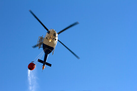 Mountain firefighting helicopter, heading to a fire spilling water from a basket it carries.