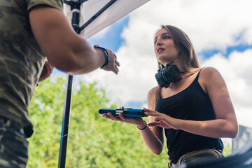 Naklejka premium Outdoor shot of gun reseller. Long-haired caucasian young adult girl in a black tank top holding a black gun and talking to the seller. Beautiful sunny weather. High quality photo