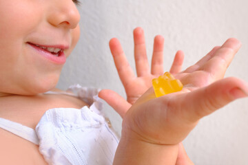 small child smiles openly, blonde girl 3 years old wants to eat gelatinous sweets, gummy bear, kid...