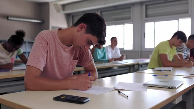 Hispanic latin college students studying and doing exercises in classroom. Concentrated teenage boy answering exam questions. High quality 4k footage