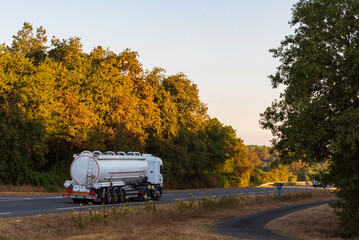 Fuel tanker truck driving along a conventional highway, surrounded by trees.