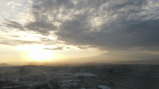 aerial time lapse of a dusty town at sunset cludy with volcano popocatepetl at the background, in Mexico