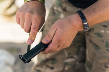 Gunsmithing concept. Two hands of an unrecognizable caucasian man in moro pants showing a black part of a gun or a rifle to the camera. Outdoor closeup shot. High quality photo