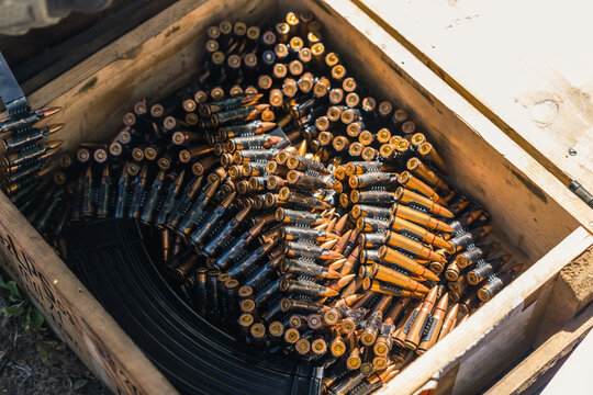 Big wooden box full of shiny golden rifle bullet tapes for machine guns. Sunshine. Outdoor shot. Military equipment concept. High quality photo