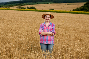Young farmer woman in straw hat and checkered shirt on wheat ripe golden field. Agriculture. Wheat ripens
